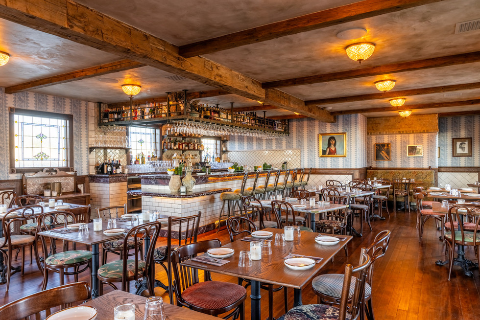 Warmly lit Bacari North Park dining room with wooden tables, exposed beams and a central bar.