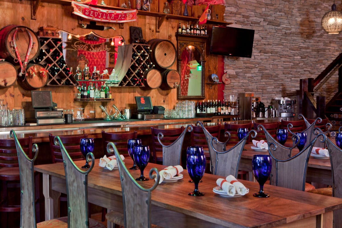 Wooden dining tables with blue goblets beside the tapas bar at Café Sevilla San Diego