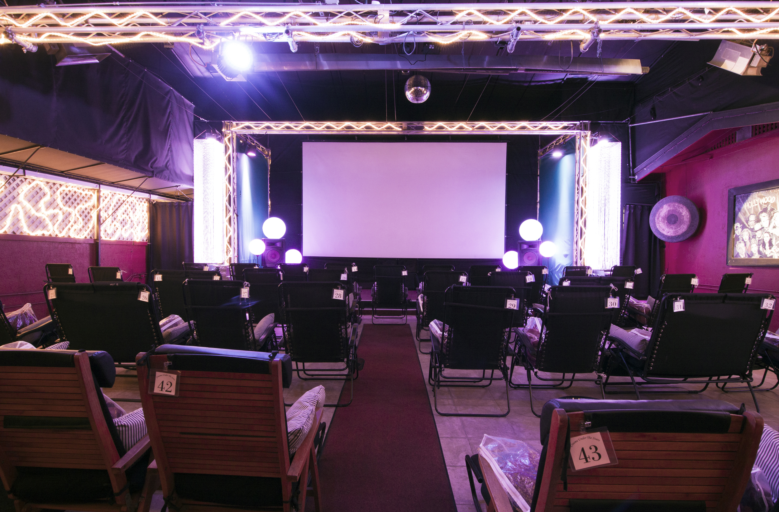 Reclining seats face a large projection screen under purple lighting at Cinema Under the Stars in Mission Hills.