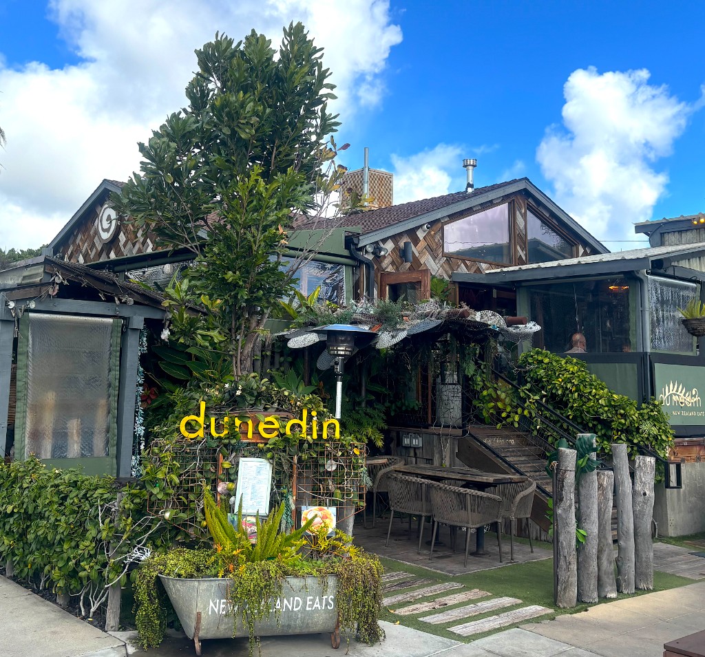 Dunedin entrance with its yellow neon sign, greenery and outdoor seating in North Park