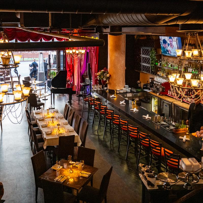 Il Sogno Italiano’s dining tables, bar, chandeliers, and grand piano beneath red curtains