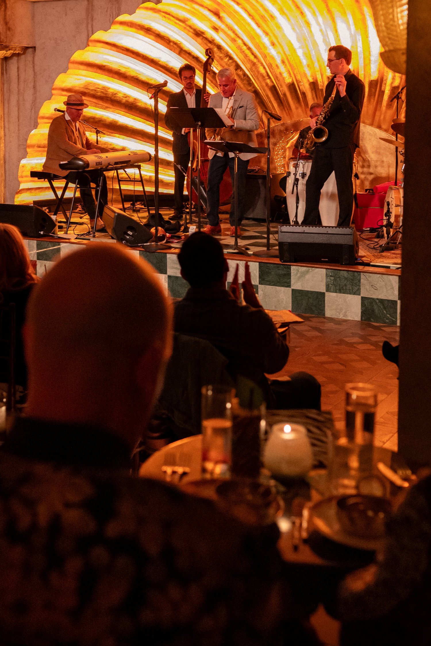Jazz musicians performing on the gold clamshell stage at Lou Lou’s, with seated diners in the foreground