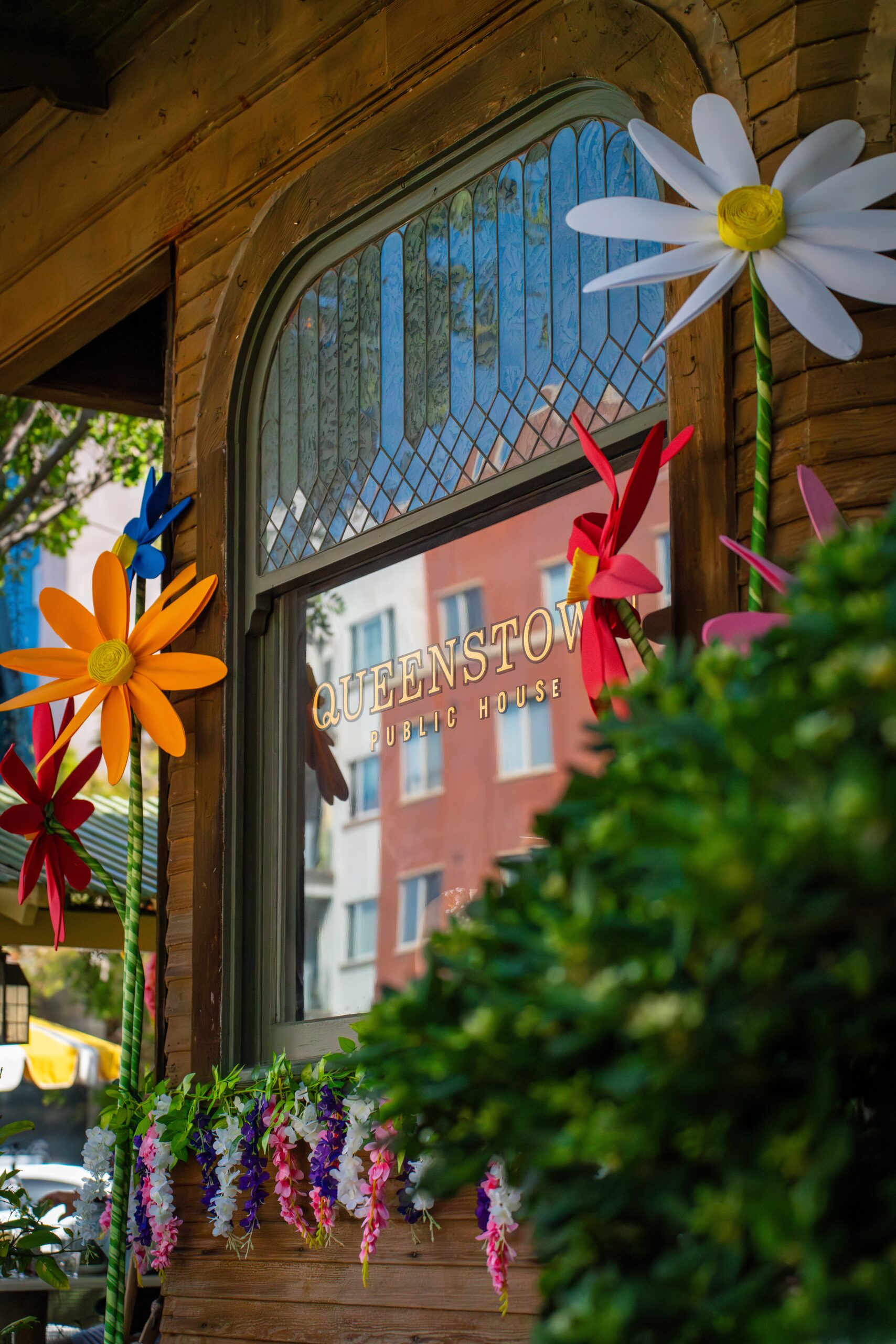 Queenstown Public House lettering on its cottage window, surrounded by colorful flower decorations